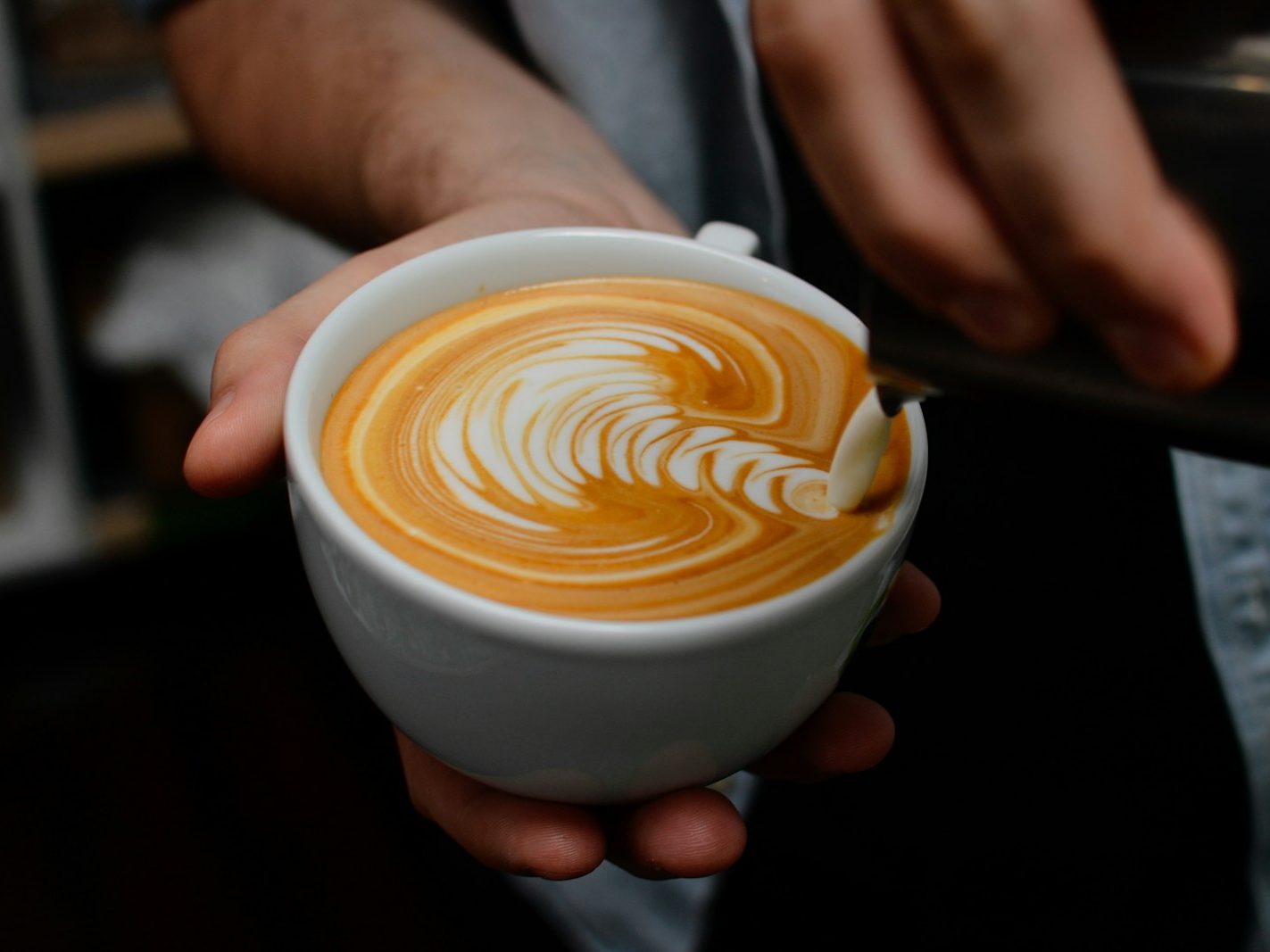 A barista's hands finishing latte art in a white cup