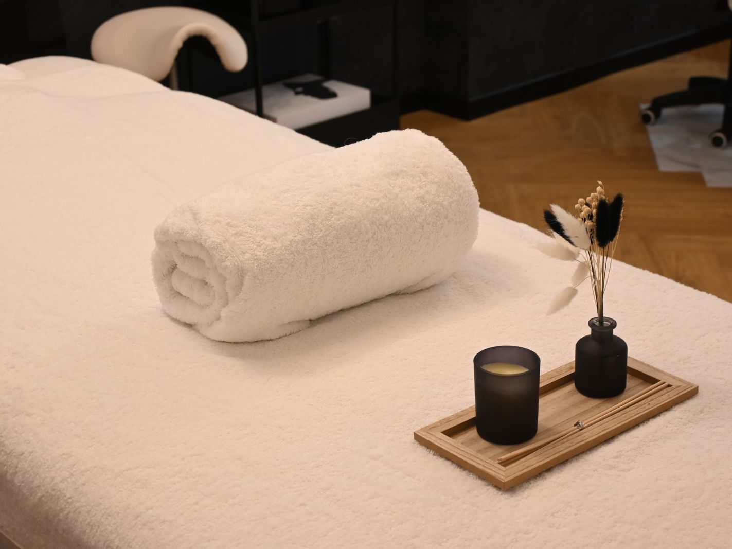 A massage table set with a rolled white towel, a candle and a small vase of dried stems